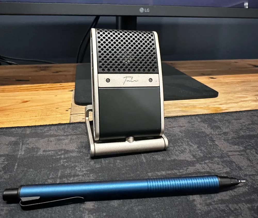 A Tula microphone on a stand in front of a monitor, with a blue pen in the foreground for scale